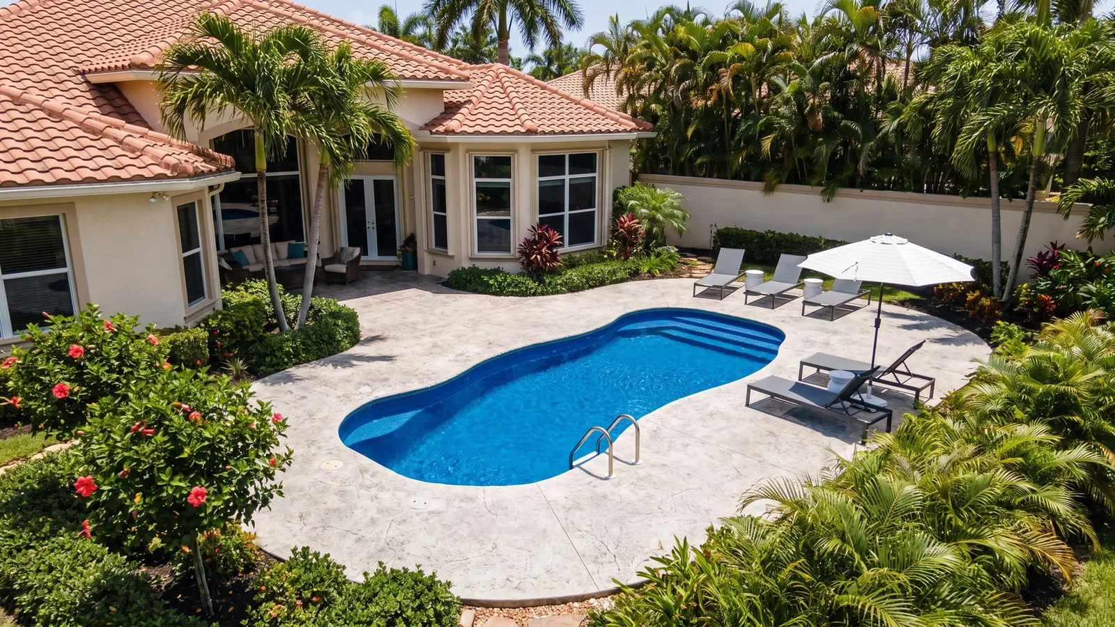 An elevated view of a blue pool, sun loungers, and surrounding palms.